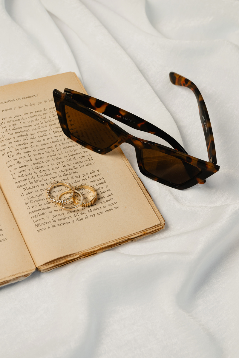 Brown Sunglasses, Book and Gold Rings on White Silk